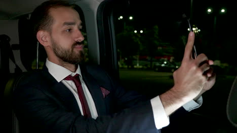 Happy-businessman-taking-a-selfie-in-the-back-seat-of-his-luxury-car-with-personal-driver