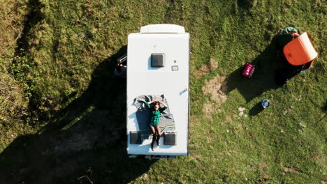Top-view-from-drone-of-beautiful-young-woman-relaxing-on-top-of-camper-van