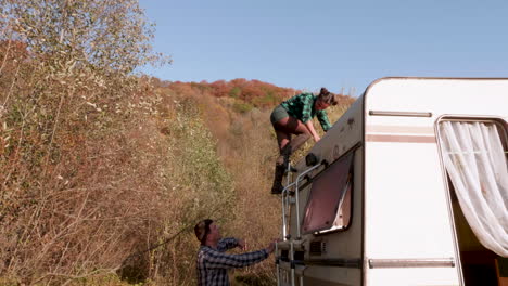Beautiful-caucasian-young-woman-getting-down-from-the-top-of-her-camper-van