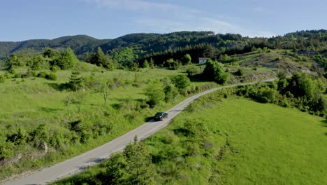 Aerial-tracking-shot-of-black-car-on-road-in-idyllic-green-Rhodope-Mountains-of-Bulgaria-during-summer
