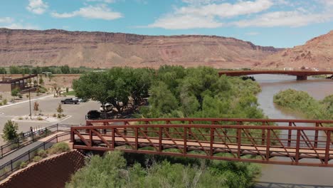 Aerial-of-pedestrian-bridge-over-the-Colorado-River-near-Moab,-and-in-distance-visible-Bridge-of-US-191---stands-as-a-testament-to-engineering-and-nature's-majesty