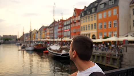 Man-enjoying-sunset-from-bridge-in-Nyhavn-with-view-of-boats-and-colorful-townhouses