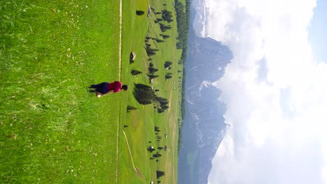 Rear-shot-of-woman-standing-in-meadow-taking-her-hat-off-with-Seiser-Alm-mountains-in-background