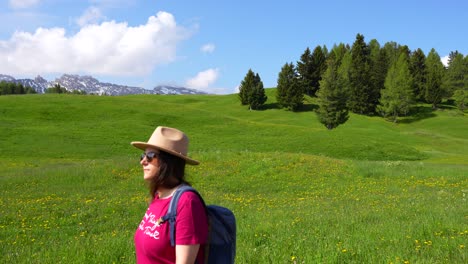 Woman-with-sunglasses-walking-along-a-green-meadow-in-Alpe-di-Siusi,-Italy