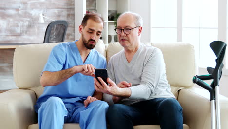 Krankenpfleger-Hilft-Einem-Pensionierten-Alten-Mann,-Ein-Smartphone-Zu-Benutzen
