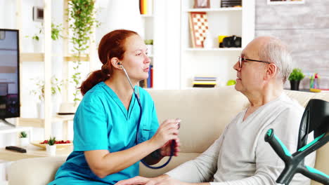 Caucasian-female-nurse-listening-to-elderly-retired-man-heartbeat-in-bright-and-cozy-nursing-home