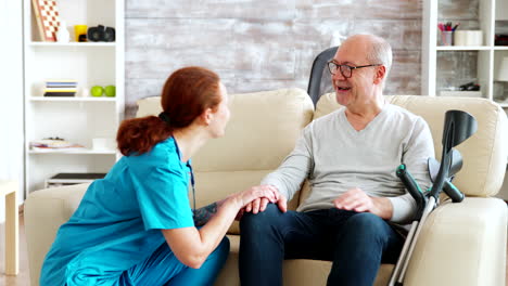 Female-nurse-talking-and-taking-care-of-old-disabled-man-sitting-on-the-sofa