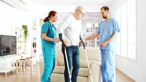 Two-nurses-helping-an-old-disabled-man-with-crutches-to-walk-in-his-room