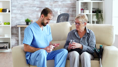 Male-nurse-sitting-on-couch-with-senior-woman-giving-her-medical-treatment-in-nursing-home