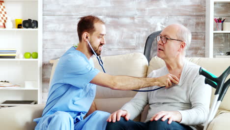 Revealing-shot-of-young-male-nurse-listening-to-old-retired-man-heartbeat