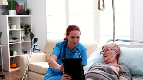 Anciana-Acostada-En-La-Cama-Aprendiendo-De-Una-Doctora-A-Usar-Una-Tableta