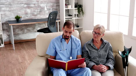 Male-nurse-in-retirement-home-reading-a-book-to-elderly-woman