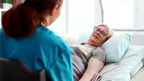 In-nursing-home-old-sick-lady-lying-in-bed-talks-with-a-female-nurse