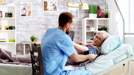 In-retirement-home-male-nurse-checks-old-sick-lady-blood-pressure