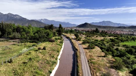 Aerial-of-water-canal-next-to-road-overlooking-scenic-idyllic-relaxing-mountainous-countryside-in-rural-area-of-Chile