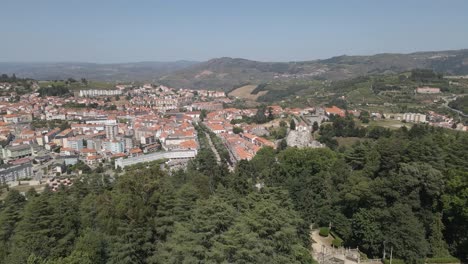 Aerial-view-of-Lamego-city,-drone-flying-over-the-pine-trees-forest-with-Lamego-city-on-the-background