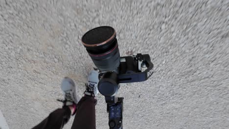 POV-Looking-Down-At-Camera-On-Gimbal-Stabiliser-In-Underslung-Mode-Filming-Along-Street-Pavement