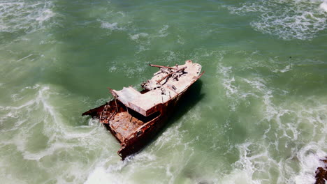Aerial-orbit-around-rusted-old-shipwreck-lying-on-rocky-shallows,-Cape-Agulhas