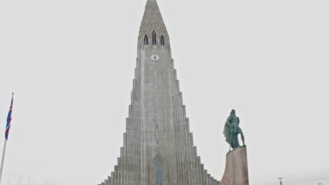 Inclinación-De-La-Iglesia-Hallgrímskirkja-Con-Turistas-En-La-Plaza-Y-La-Estatua-De-Leif-Erikson-Frente-Al-Edificio-Alto