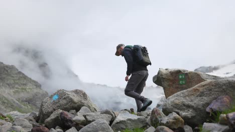 Male-Hiker-Climbing-Over-Rocks-In-In-Valmalenco-Region-In-Italy-With-Mountain-Clouds-In-Background