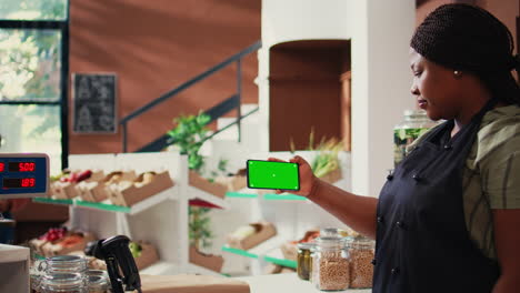 Storekeeper-holds-mobile-phone-with-greenscreen-display