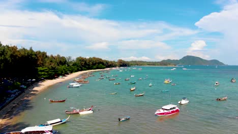 Pedestal-aerial-drone-shot-of-the-expanse-and-length-of-Rawai-beachfront,-showing-a-number-of-speed-boats,-kayaks,-wooden-long-tailed-boats,-and-a-scenic-view-of-the-Andaman-Sea,-in-Phuket,-Thailand