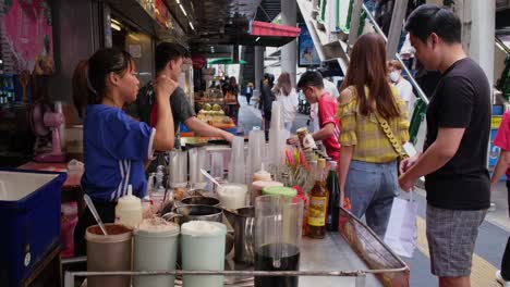 Vendors-selling-drinks-to-commuters-during-a-hot-day-at-the-sidewalk-near-the-stairs-going-up-Phrom-Phong-BTS-station,-Street-Food-along-Sukhumvit-Road-in-Bangkok,-Thailand