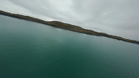 Aerial-FPV-drone-flight-over-drifting-icebergs-in-a-glacial-lagoon-in-Jokulsarlon-Bay,-Iceland