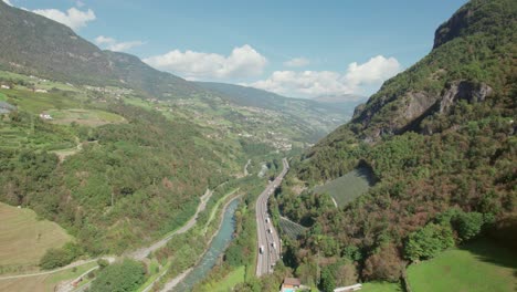 Autopista-Que-Atraviesa-La-Montaña-Junto-Al-Río,-Autos-Que-Van-Al-Túnel,-Vista-De-Drones,-Clima-Soleado