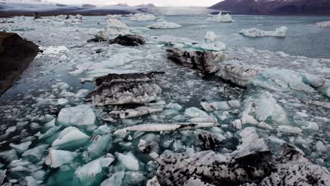 Large-chunks-of-ice-in-glacial-lake-Jökulsárlón,-Iceland,-aerial-descend-tilt-up