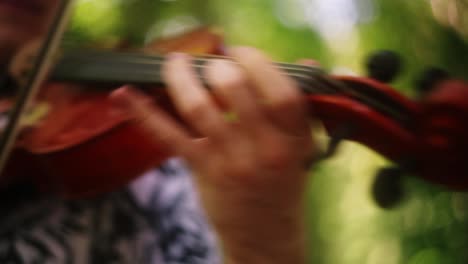 Caucasian-violinist-strokes-string-with-bow-outdoors-in-forest,-symphony-concert