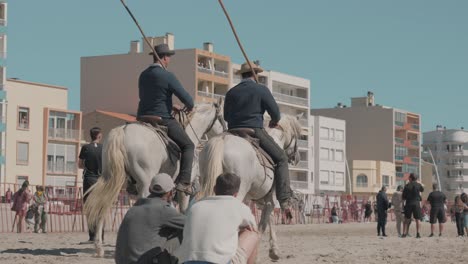 Feria-in-Palavas,-men-riding-horses-on-crowded-tourist-beach-in-southern-France