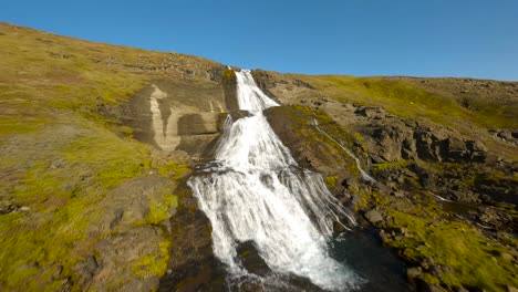FPV-aerial-footage-of-the-large-Glymor-waterfall,-flying-upwards-stream-in-scenic-landcape,-Iceland