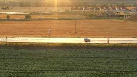 A-silver-car-moving-through-a-beautiful-countryside-at-sunset---Aerial-drone-shot