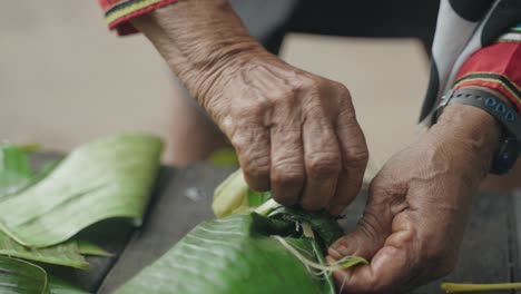 Closeup-of-Hands-making-a-knot-into-Banana-leaves,-sealing-them-to-put-it-over-fire,-Peru