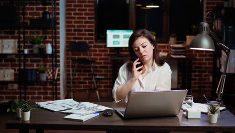 Woman-answering-phone-call-while-working-in-office-at-computer-desk