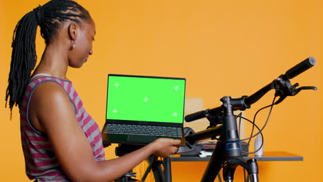 Cheerful-woman-following-tutorial-videos-on-chroma-key-laptop,-learning-to-fix-bike