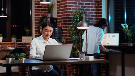 Cheerful-staff-member-looking-over-accounting-figures-on-laptop-screen-at-night
