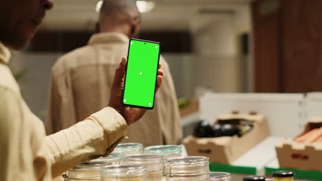 African-american-storekeeper-holding-phone-with-greenscreen-in-grocery-store