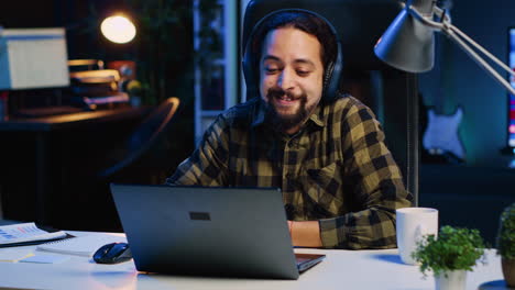 Cheerful-man-relaxing-at-home-by-watching-TV-show-on-laptop-using-headphones