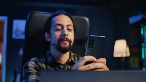 Happy-man-at-home-texting-friend-on-cellphone,-taking-break-from-remote-job
