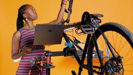 Technician-with-laptop-in-hand-analyzing-broken-bike-over-studio-background