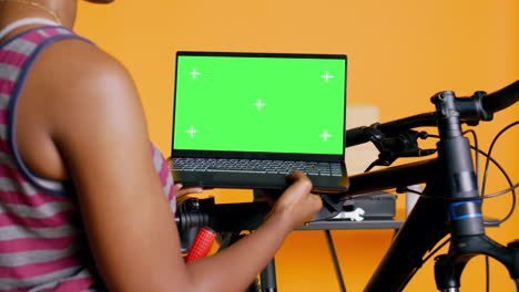 Cheerful-mechanic-doing-bike-servicing,-looking-on-green-screen-laptop