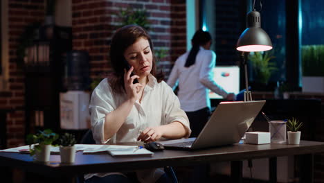 Woman-answering-phone-call-while-working-in-office-at-computer-desk