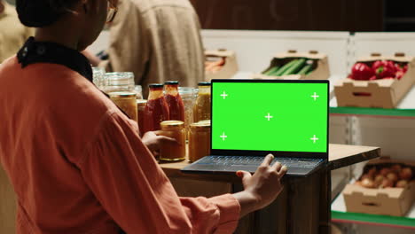 Vendor-looks-at-greenscreen-on-laptop-while-preparing-merchandise