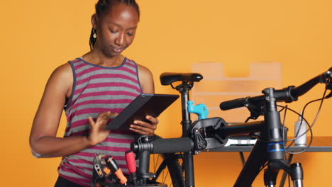 Mujer-Feliz-Divirtiéndose-Reparando-Componentes-De-Bicicletas-Siguiendo-Un-Tutorial-En-Tableta
