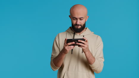 Fröhlicher-Muslimischer-Mann,-Der-Im-Studio-Mobile-Videospiele-Spielt