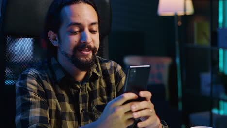 Smiling-man-at-home-texting-best-friend-on-smartphone,-taking-break-from-work