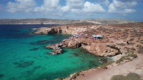Tourists-Swimming-and-Sunbathing-on-Rocks-of-Blue-Lagoon,-Comino-Island,-Malta