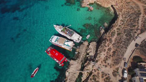 Aerial-Overhead-of-Tourist-Day-Trip-Ferry-Boats,-Revealing-Blue-Lagoon-on-Comino-Island,-Malta